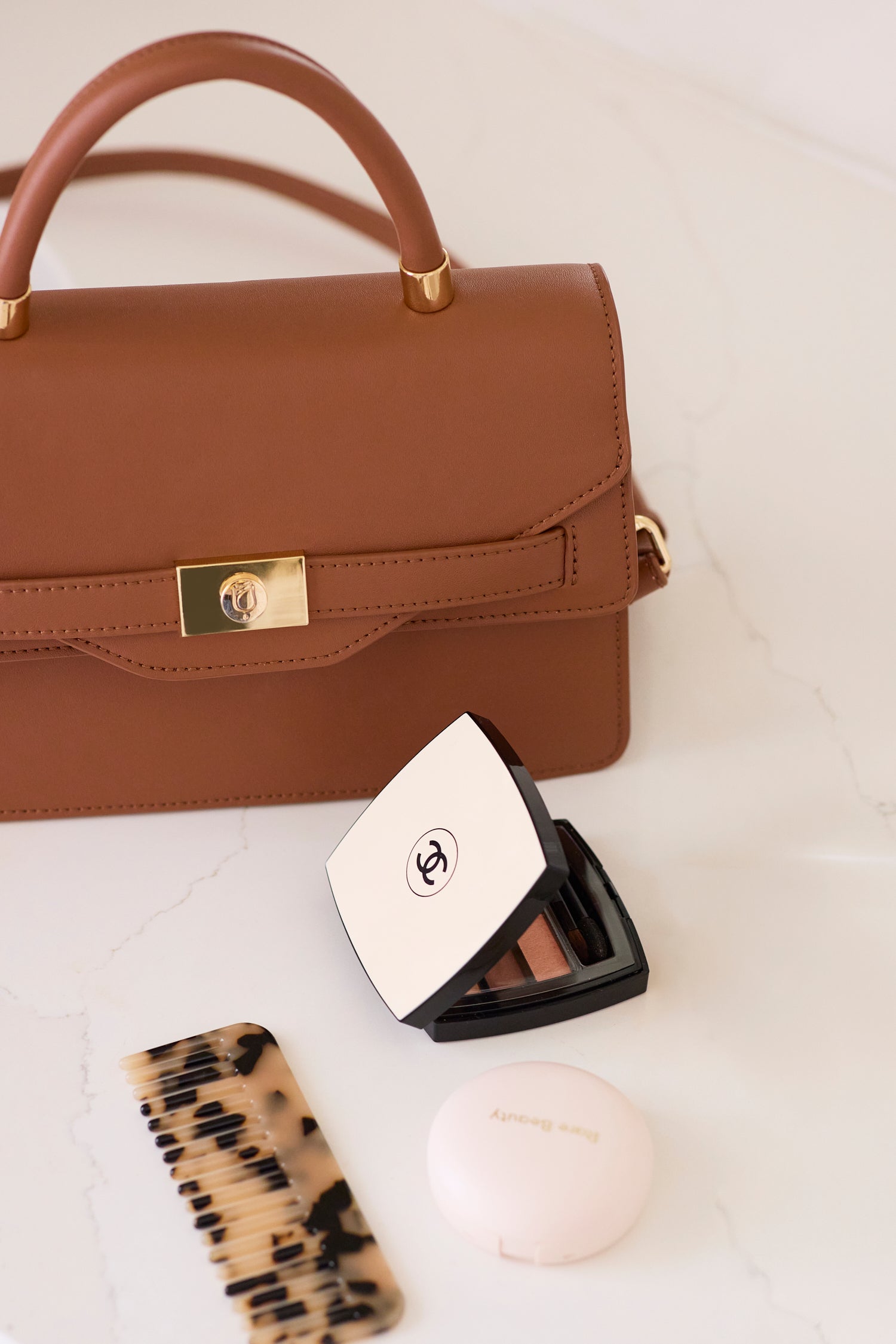 Brown handbag with makeup items including a compact and a brush on a light surface.